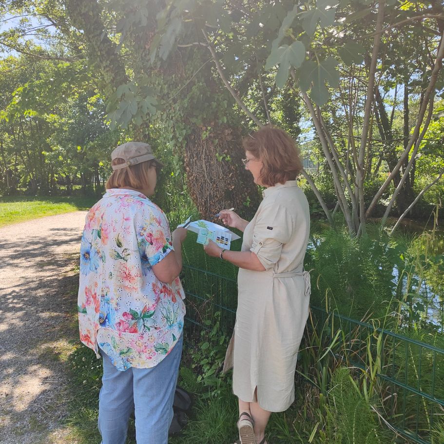 Atelier carnet de voyage en extérieur : moi expliquant une technique d’aquarelle à une élève dans un parc